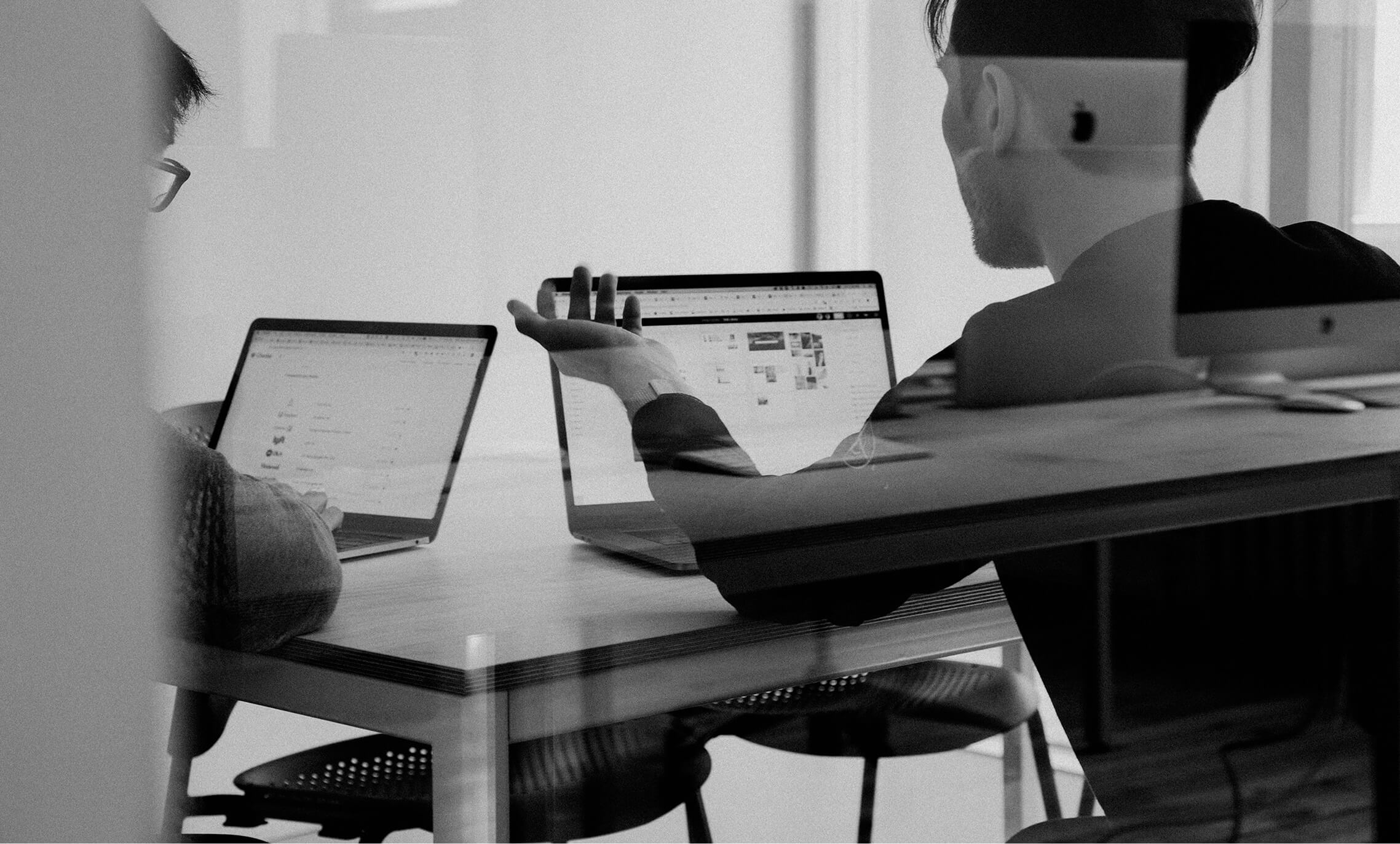 Black and white image of people working at a table with laptops, showing hands gesturing during discussion of digital content displayed on screens, with inspologo in the corner.